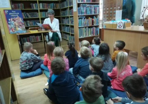 Dzieci słuchają opowiadania czytanego przez panią bibliotekarkę.